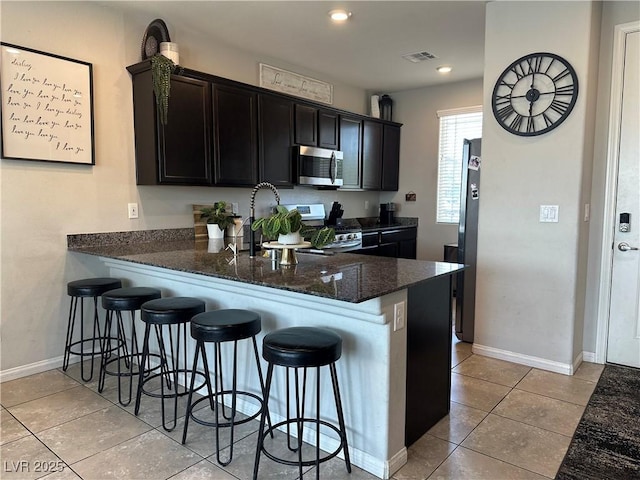 7636 Bandon Cliffs St, North Las Vegas, NV 89084 - kitchen with appliances with stainless steel finishes, dark stone counters, a breakfast bar, light tile patterned flooring, and recessed lighting