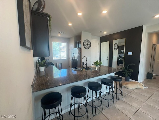 7636 Bandon Cliffs St, North Las Vegas, NV 89084 - kitchen featuring a peninsula, stainless steel fridge with ice dispenser, dark stone counters, light tile patterned floors, and recessed lighting