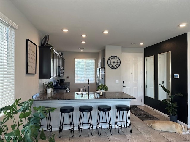 7636 Bandon Cliffs St, North Las Vegas, NV 89084 - kitchen with stainless steel appliances, a peninsula, a breakfast bar, dark stone countertops, and recessed lighting