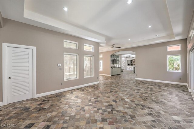 2017 Slow Wind St, Las Vegas, NV 89134 - unfurnished living room featuring arched walkways, a tray ceiling, recessed lighting, stone finish floors, and ceiling fan