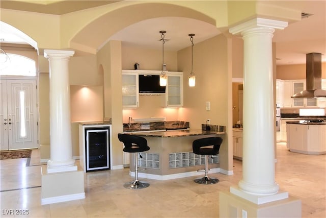 7250 Birkland Ct, Las Vegas, NV 89117 - kitchen with wall chimney range hood, ornate columns, beverage cooler, and a breakfast bar area