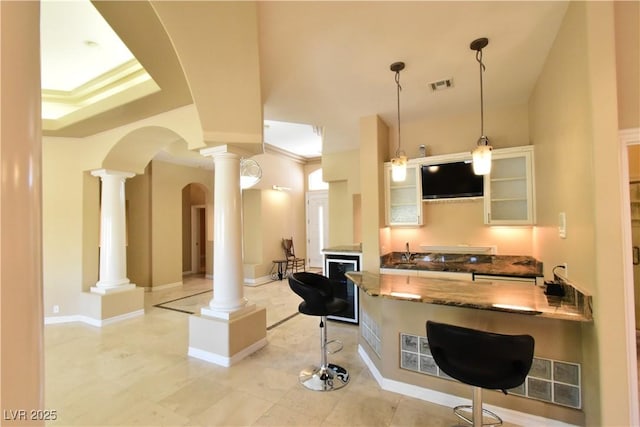 7250 Birkland Ct, Las Vegas, NV 89117 - kitchen featuring ornate columns, dark stone counters, glass insert cabinets, a breakfast bar area, and beverage cooler