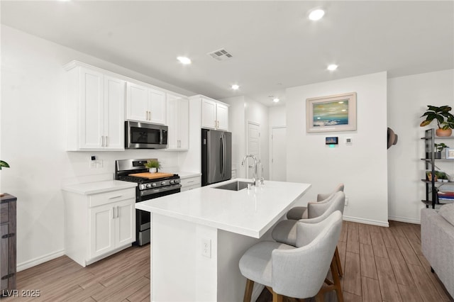 9743 Mojave Mountain St, Las Vegas, NV 89166 - kitchen with appliances with stainless steel finishes, light wood-style flooring, a center island with sink, a breakfast bar area, and white cabinets