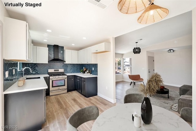 5004 Celebrity Cir, Las Vegas, NV 89119 - kitchen featuring gas stove, wall chimney exhaust hood, light wood-style flooring, tasteful backsplash, and white cabinetry