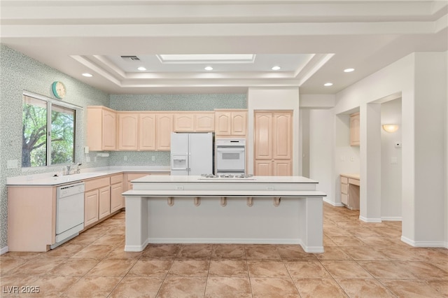 10548 Findlay Ave, Las Vegas, NV 89134 - kitchen featuring white appliances, a tray ceiling, light brown cabinetry, and a center island with sink