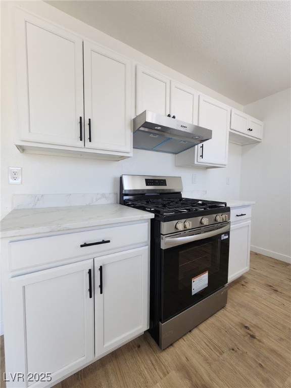 3318 Covey Ln, Las Vegas, NV 89115 - kitchen featuring stainless steel gas stove, under cabinet range hood, light wood-style floors, white cabinets, and light stone countertops
