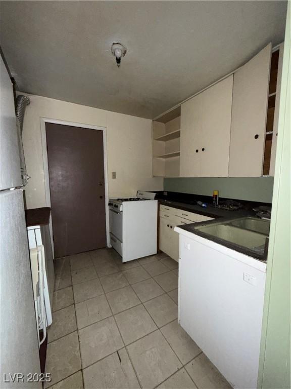 1104 High St, Ely, NV 89301 - kitchen with white range with gas cooktop, open shelves, dark countertops, freestanding refrigerator, and light tile patterned floors