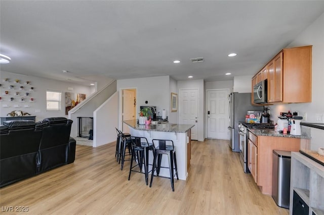 8733 Autumn Teal Ave, Las Vegas, NV 89178 - kitchen featuring appliances with stainless steel finishes, a breakfast bar area, light wood finished floors, dark stone countertops, and recessed lighting