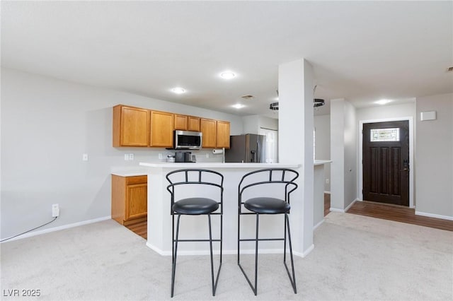 700 Red Bark Ln, Henderson, NV 89011 - kitchen featuring appliances with stainless steel finishes, light carpet, a breakfast bar, a peninsula, and brown cabinetry