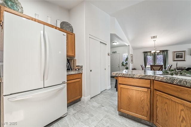3495 Eagle Bend St, Las Vegas, NV 89122 - kitchen featuring freestanding refrigerator, vaulted ceiling, brown cabinets, hanging light fixtures, and a chandelier