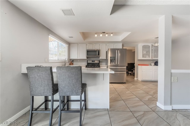 327 Fuente Dr, Henderson, NV 89014 - kitchen featuring stainless steel appliances, a raised ceiling, a kitchen breakfast bar, a peninsula, and white cabinetry
