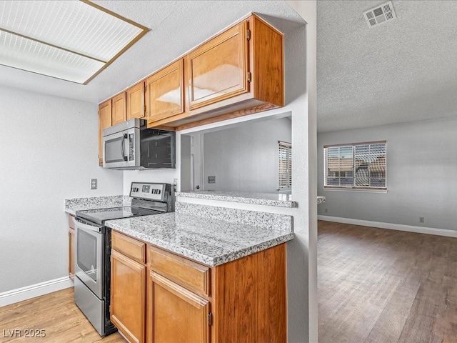 5861 Medallion Dr Unit 202, Las Vegas, NV 89122 - kitchen with appliances with stainless steel finishes, light wood-style flooring, brown cabinetry, light stone counters, and a textured ceiling