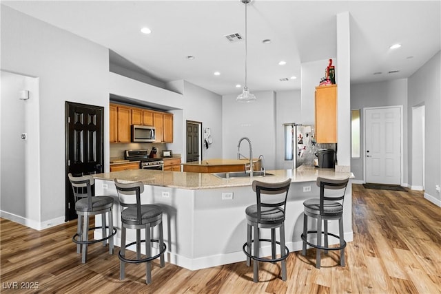 4212 Helens Pouroff Ave, North Las Vegas, NV 89085 - kitchen featuring stainless steel appliances, a breakfast bar area, light wood-style floors, brown cabinetry, and a peninsula