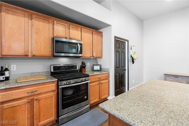 4212 Helens Pouroff Ave, North Las Vegas, NV 89085 - kitchen featuring appliances with stainless steel finishes, light stone countertops, brown cabinetry, and wood finished floors