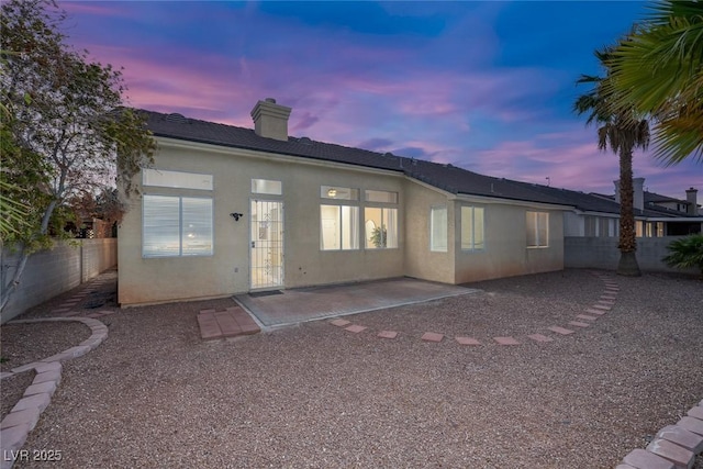 5512 Goldbrush St, Las Vegas, NV 89130 - back of property at dusk featuring a patio area, stucco siding, a fenced backyard, and a chimney