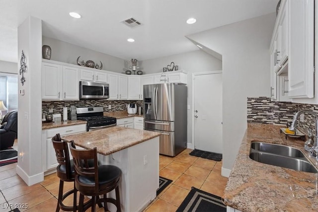 10918 Avenzano St, Las Vegas, NV 89141 - kitchen featuring appliances with stainless steel finishes, decorative backsplash, white cabinetry, a kitchen island, and a kitchen breakfast bar