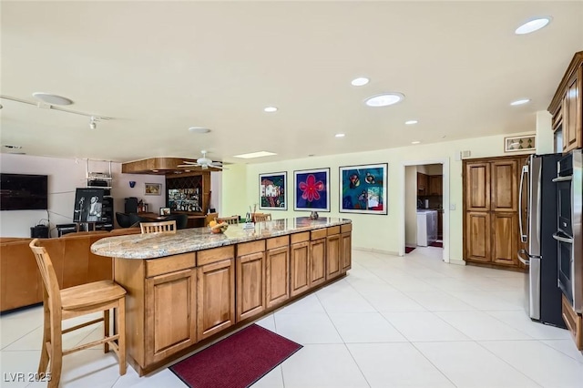 2770 La Casita Ave, Las Vegas, NV 89120 - kitchen featuring light stone countertops, brown cabinetry, open floor plan, a ceiling fan, and a kitchen island