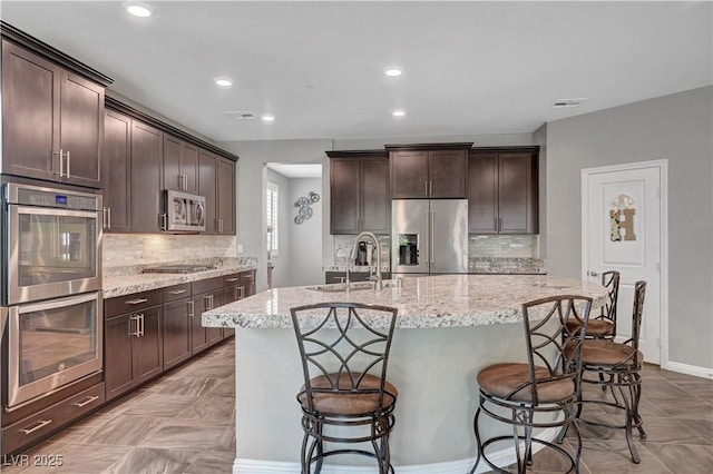 2433 Amatrice St, Henderson, NV 89044 - kitchen featuring stainless steel appliances, backsplash, dark brown cabinets, light stone counters, and recessed lighting