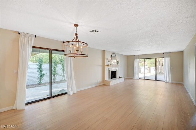 1905 Plaza Del Padre, Las Vegas, NV 89102 - unfurnished living room featuring a chandelier, light wood-type flooring, a textured ceiling, and a fireplace with raised hearth