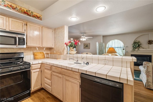 7950 W Flamingo Rd Unit 1024, Las Vegas, NV 89147 - kitchen featuring black appliances, a peninsula, light brown cabinets, open floor plan, and light wood finished floors