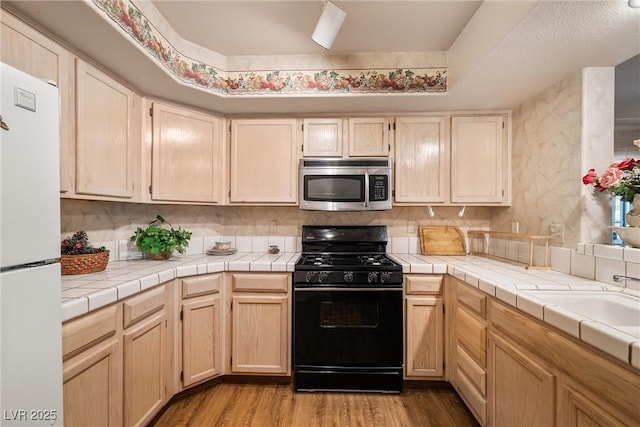 7950 W Flamingo Rd Unit 1024, Las Vegas, NV 89147 - kitchen with stainless steel microwave, black gas range, freestanding refrigerator, light wood finished floors, and light brown cabinets