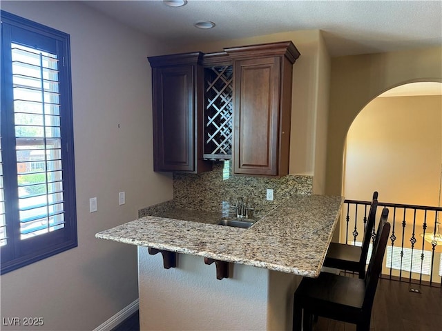 585 Via Alhambra, Las Vegas, NV 89123 - kitchen with a breakfast bar, tasteful backsplash, arched walkways, light stone counters, and dark wood-style floors