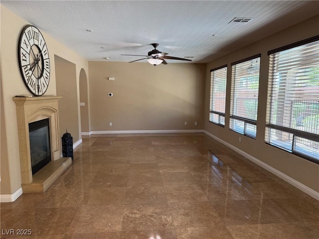 585 Via Alhambra, Las Vegas, NV 89123 - unfurnished living room featuring a ceiling fan, arched walkways, a glass covered fireplace, and a textured ceiling