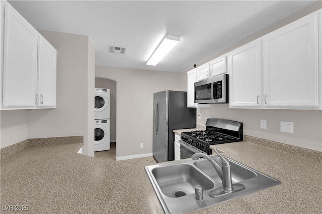 9957 Fine Fern St, Las Vegas, NV 89183 - kitchen with appliances with stainless steel finishes, stacked washer / drying machine, and white cabinetry
