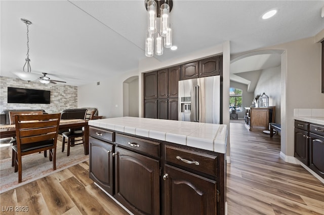 5452 Desert Spring Rd, Las Vegas, NV 89149 - kitchen featuring arched walkways, high end fridge, dark brown cabinetry, tile counters, and wood finished floors