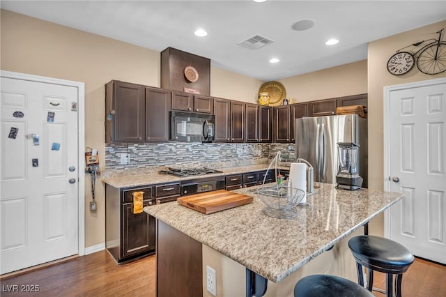 10312 Glimmering Star Dr, Las Vegas, NV 89178 - kitchen featuring appliances with stainless steel finishes, a kitchen bar, dark brown cabinetry, light wood-style floors, and light stone countertops