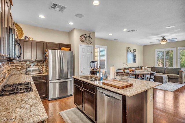 10312 Glimmering Star Dr, Las Vegas, NV 89178 - kitchen featuring stainless steel appliances, open floor plan, light wood-style flooring, dark brown cabinets, and a center island with sink