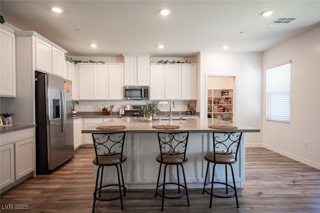 9256 Alden Pointe Ct, Las Vegas, NV 89143 - kitchen with appliances with stainless steel finishes, a breakfast bar, a center island with sink, dark wood-type flooring, and white cabinetry