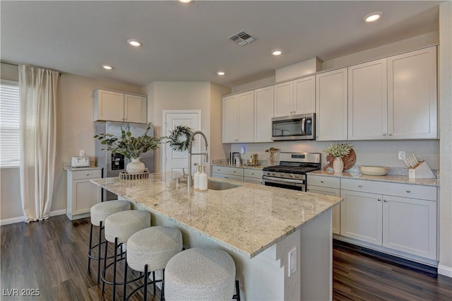 7705 Alder Forest St, Las Vegas, NV 89113 - kitchen featuring appliances with stainless steel finishes, dark wood-style floors, light stone countertops, an island with sink, and a breakfast bar