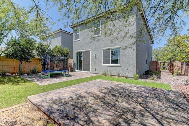 7705 Alder Forest St, Las Vegas, NV 89113 - back of house featuring a trampoline, a patio, a fenced backyard, and stucco siding
