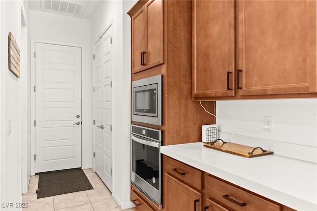 10160 Tree Blossom Ave, Las Vegas, NV 89166 - kitchen featuring stainless steel appliances, light countertops, light tile patterned floors, and brown cabinetry