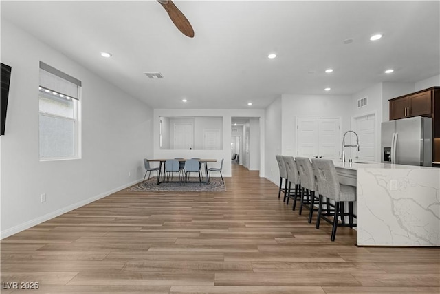 5936 Bruselas St, Las Vegas, NV 89113 - kitchen with stainless steel fridge, recessed lighting, a kitchen bar, light stone counters, and light wood finished floors