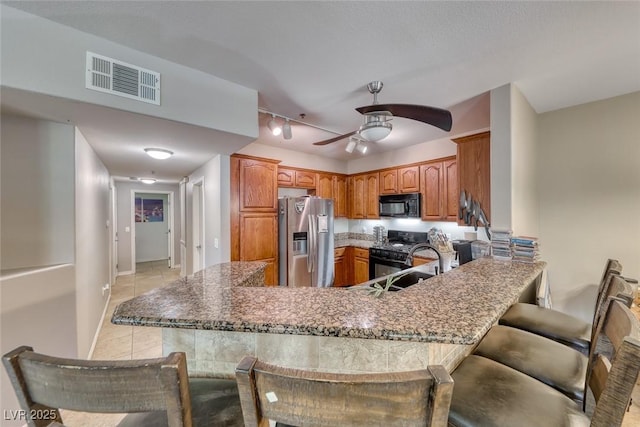 105 Lighthouse Dr Unit 105, Boulder City, NV 89005 - kitchen with black appliances, a peninsula, ceiling fan, brown cabinets, and light tile patterned flooring