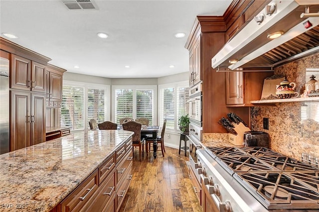 5224 Painted Lakes Way, Las Vegas, NV 89149 - kitchen with exhaust hood, stainless steel appliances, dark wood-style flooring, light stone countertops, and backsplash