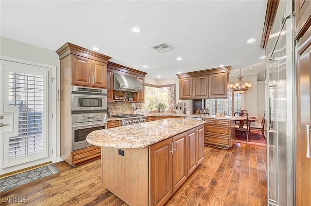 5224 Painted Lakes Way, Las Vegas, NV 89149 - kitchen featuring stainless steel appliances, range hood, wood finished floors, light stone countertops, and a kitchen island
