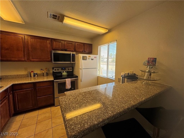 5499 Indian River Dr Unit 356, Las Vegas, NV 89103 - kitchen with stainless steel appliances, a peninsula, light tile patterned floors, a breakfast bar area, and a textured ceiling
