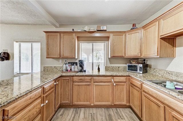 744 Mcknight St, Las Vegas, NV 89101 - kitchen featuring light wood-type flooring, healthy amount of natural light, stainless steel microwave, light stone countertops, and a textured ceiling