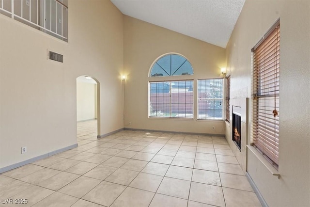 1711 Ember Glow Cir, Las Vegas, NV 89119 - unfurnished living room featuring a lit fireplace, light tile patterned floors, high vaulted ceiling, and arched walkways