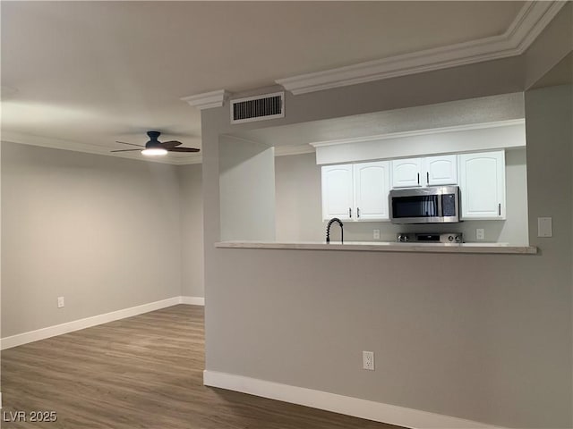 8101 W Flamingo Rd Unit 1102, Las Vegas, NV 89147 - kitchen with stainless steel microwave, ornamental molding, white cabinetry, wood finished floors, and ceiling fan