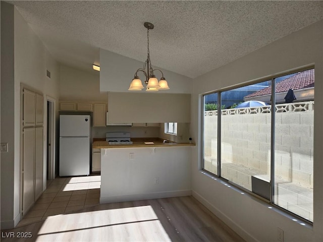 6636 Old Oxford Ave, Las Vegas, NV 89108 - kitchen with white appliances, vaulted ceiling, a textured ceiling, a chandelier, and a peninsula