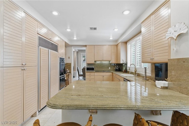 8215 Crow Valley Ln, Las Vegas, NV 89113 - kitchen featuring light brown cabinetry, a peninsula, black appliances, decorative backsplash, and a kitchen bar