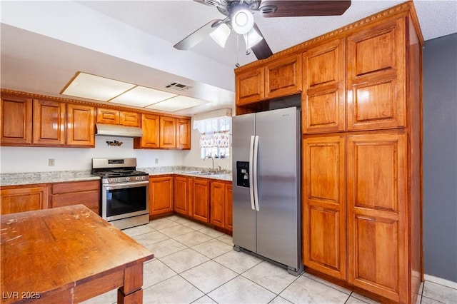 5673 Coaldale Pl, Las Vegas, NV 89110 - kitchen featuring stainless steel appliances, under cabinet range hood, brown cabinetry, light tile patterned flooring, and a ceiling fan