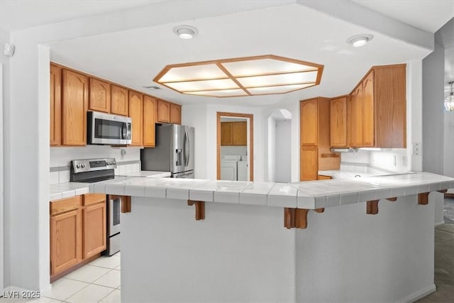 5981 Doubletree Rd, Pahrump, NV 89061 - kitchen featuring stainless steel appliances, washer and clothes dryer, a peninsula, a breakfast bar, and tile counters