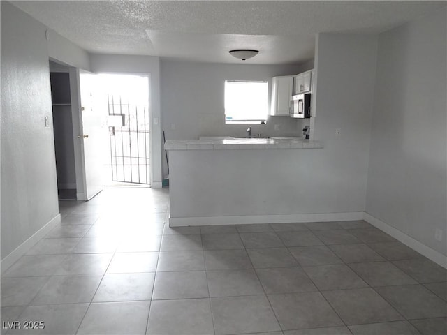 5388 Swenson St Unit 26, Las Vegas, NV 89119 - kitchen featuring stainless steel microwave, light countertops, a textured ceiling, a peninsula, and white cabinetry