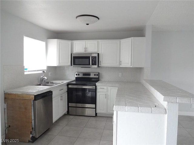5388 Swenson St Unit 26, Las Vegas, NV 89119 - kitchen featuring appliances with stainless steel finishes, a peninsula, white cabinetry, tasteful backsplash, and light tile patterned floors
