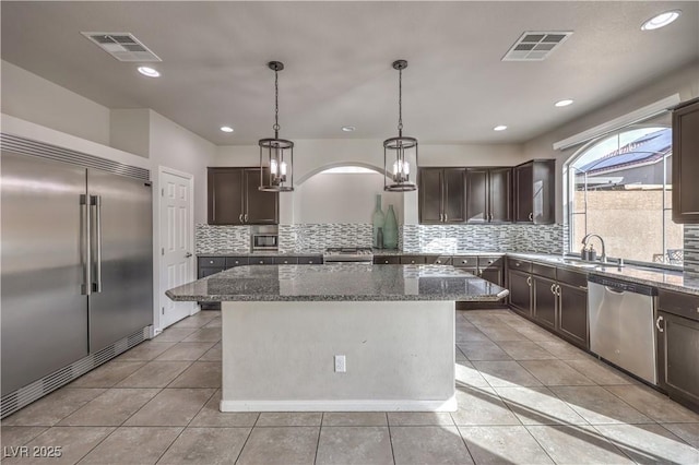 9876 Parador Cellars Ct, Las Vegas, NV 89141 - kitchen featuring built in appliances, dark brown cabinets, decorative backsplash, a center island, and light tile patterned flooring